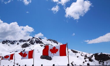Des drapeaux du Canada flottant au vent avec les montagnes enneigées en fond